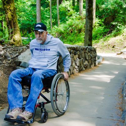 An older man wheels down a path in a forested area