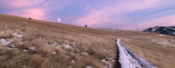 A snowy path on a hillside with a pink and purple sunset in the sky