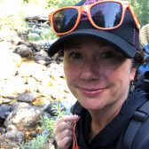 Dr. Rayna Sage, a woman wearing a ball cap on a hike in the woods